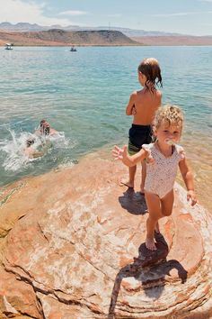 two young children are playing in the water on a rocky cliff by the beach,