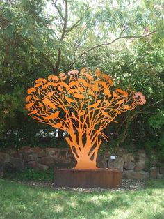 an orange sculpture in the middle of a grassy area with trees and bushes behind it