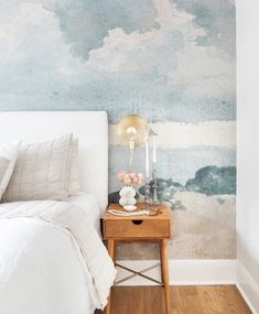 a white bed sitting next to a wooden table on top of a hard wood floor