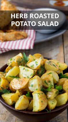 a bowl filled with potatoes and herbs on top of a wooden table next to bread