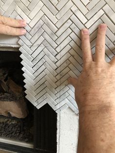 two hands reaching for something on the floor in front of a fireplace with white tiles