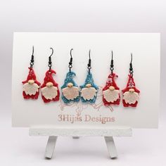 five red, white and blue gnomes are hanging from hooks on a card holder