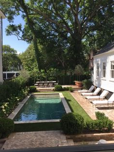 a small pool surrounded by lawn chairs and trees near a house with white sidings