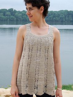 a woman standing next to the water wearing a crocheted dress