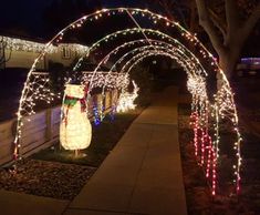 an archway covered in christmas lights with a snowman on the side walk under it