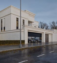 two cars are parked in front of a large white building with a garage on the side