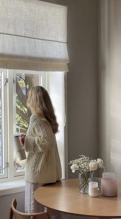 a woman standing in front of a window next to a table with flowers on it