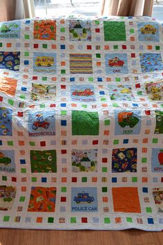 a child's quilted blanket with cars and trucks on it sitting in front of a window