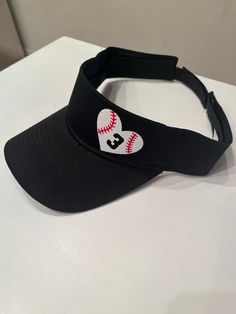 a black visor with a baseball and heart patch on the front, sitting on a white surface