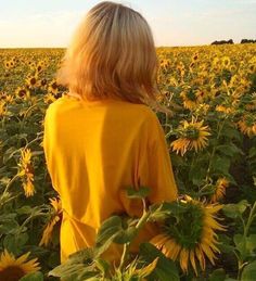 a woman standing in a field of sunflowers looking at the sky with her back to the camera