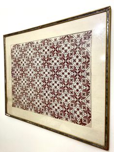 a framed piece of art hanging on the wall in front of a white wall with a red and white pattern