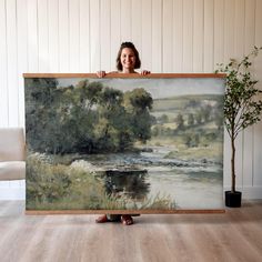 a woman is holding up a large painting