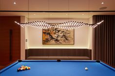 a blue pool table in front of a painting on the wall with lights hanging from it