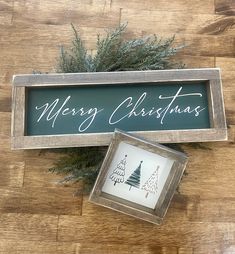 a wooden sign that says merry christmas and is next to a picture frame with a pine tree on it