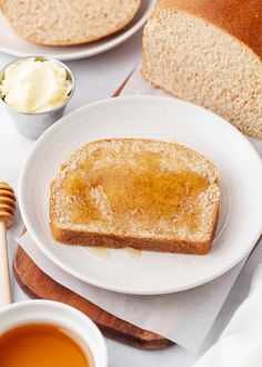 a piece of bread sitting on top of a white plate next to a bowl of honey