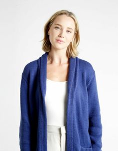 a woman standing in front of a white wall wearing a blue cardigan