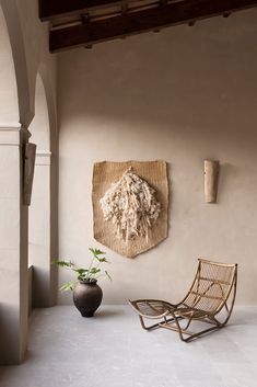 a chair sitting in front of a wall hanging on a wall next to a potted plant