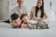 three adults and two children laying on a white bed with their arms around each other