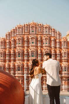 a man and woman standing in front of a large building with red tiles on it