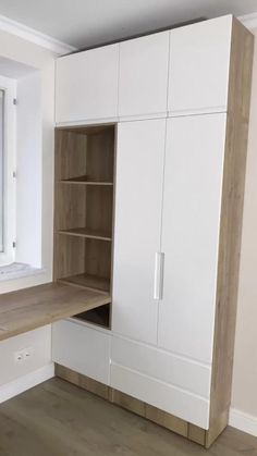 an empty room with white cupboards and wood flooring on the walls, along with a large window