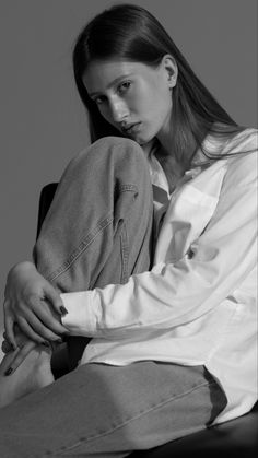 a woman sitting in a chair with her hands on her knees looking at the camera