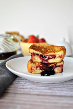 two grilled sandwiches on a white plate with fruit in the bowl and another dish behind them