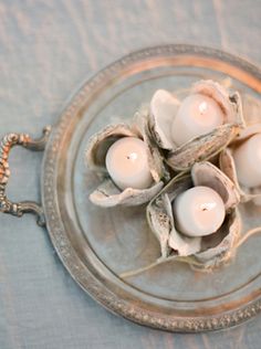 some white candles are sitting on a glass plate