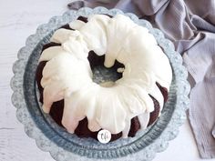 a chocolate bundt cake with white frosting on a blue plate next to a gray napkin