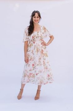 a woman in a white floral dress posing for the camera