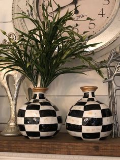 two black and white checkered vases sitting on top of a mantle next to a clock