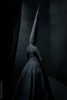 a woman in a long black dress with a knife sticking out of the back of her head