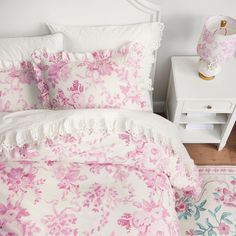 a white bed with pink flowers on it and a lamp next to the headboard