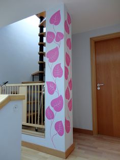 a white and pink wall with leaves painted on it in a room next to stairs