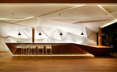 an empty bar with stools and lights on the wall behind it in a large room