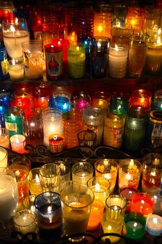 many different colored candles are lit in front of each other on a shelf with glass containers