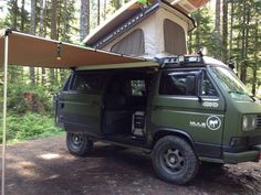 a green van is parked in the woods with its roof up and it's door open