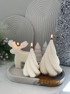 two white candles sitting on top of a table next to christmas trees and snowflakes