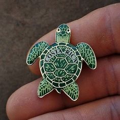 a close up of a person's hand holding a green turtle pin