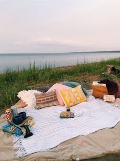 a blanket on the ground next to a body of water with books and other items sitting on it