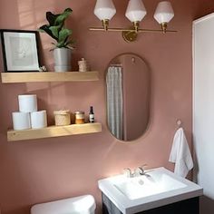 a bathroom with pink walls and shelves above the sink, toilet and mirror on the wall