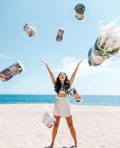 a woman standing on top of a sandy beach next to the ocean with lots of bottles in the air