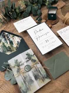 the wedding stationery is laid out on top of the wooden table with greenery