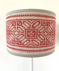 a red and white knitted lamp shade on a metal stand next to a wall