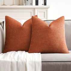 two orange pillows sitting on top of a couch next to a book shelf with books