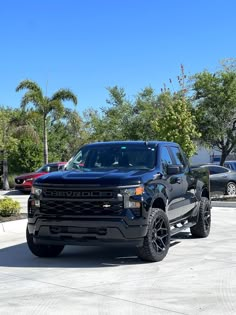 a black truck parked in a parking lot next to other cars and trees on a sunny day