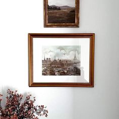 two framed pictures hang on the wall above a vase with flowers