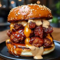 a chicken sandwich on a bun covered in cheese and sauce sitting on a black plate