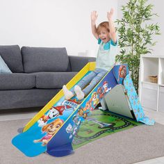 a young boy is playing on a slide in the living room with his hands up