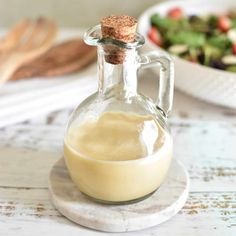 a glass bottle filled with dressing next to a bowl of salad