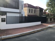 a white house with a black fence next to it on the side of a street